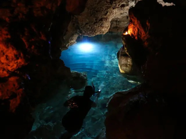 リフー島のルエンゴニの宝石と呼ばれる洞窟で、青い光に照らされた透明な水の中をシュノーケリングで進む人の様子。