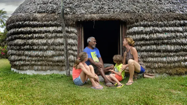 A family talks with a local host in front of a traditional hut during a tribal welcome in Lifou.