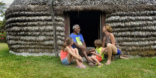 A family talks with a local host in front of a traditional hut during a tribal welcome in Lifou.