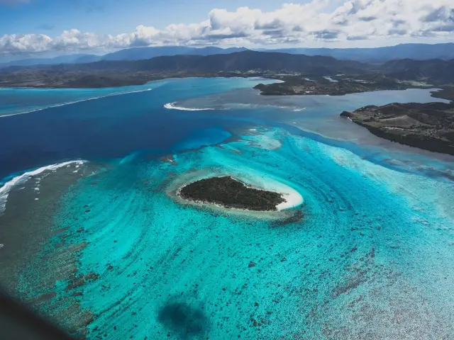 Vue aérienne de l’Île Verte entourée par les eaux turquoise du lagon de Bourail, avec le littoral et les reliefs en arrière-plan.