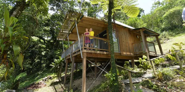 Couple sur le balcon d’un bungalow en bois sur pilotis au Ka Waboana Lodge à Hienghène, entouré d’une végétation tropicale luxuriante.