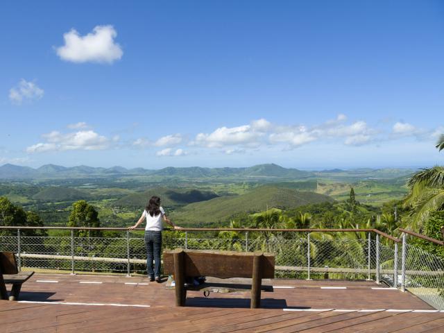 Une visiteuse contemple le panorama depuis le point de vue de Farino, avec collines verdoyantes et montagnes à l’horizon.
