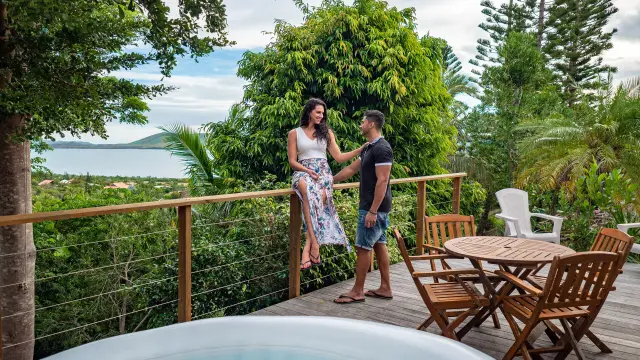 Couple on the wooden terrace at Oua-Ya Lodge in Boulouparis, with an outdoor plunge pool, garden furniture, tropical vegetation and lagoon views.