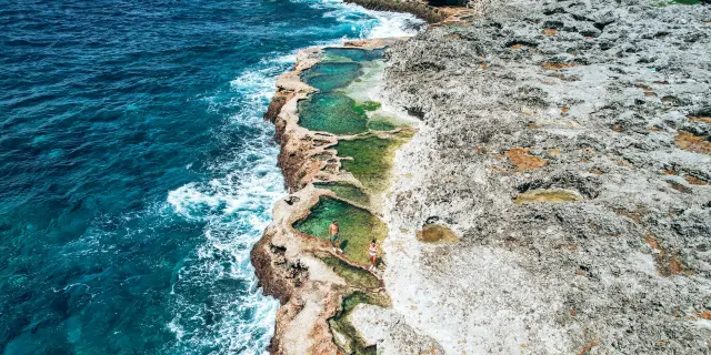 リフー島のカップ・デ・パンにある天然プールを上空から捉えた風景。海沿いの岩場にいくつもの自然の水たまりができており、澄んだ水の中で人々が過ごしている。