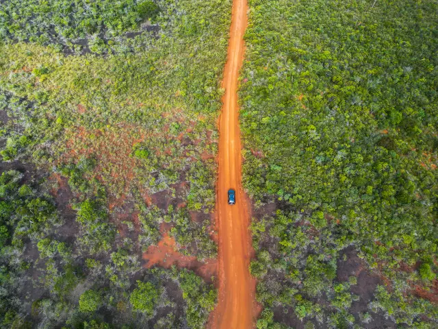 Vue aérienne d’une voiture sur une piste de terre rouge traversant la végétation du Grand Sud de la Nouvelle-Calédonie.