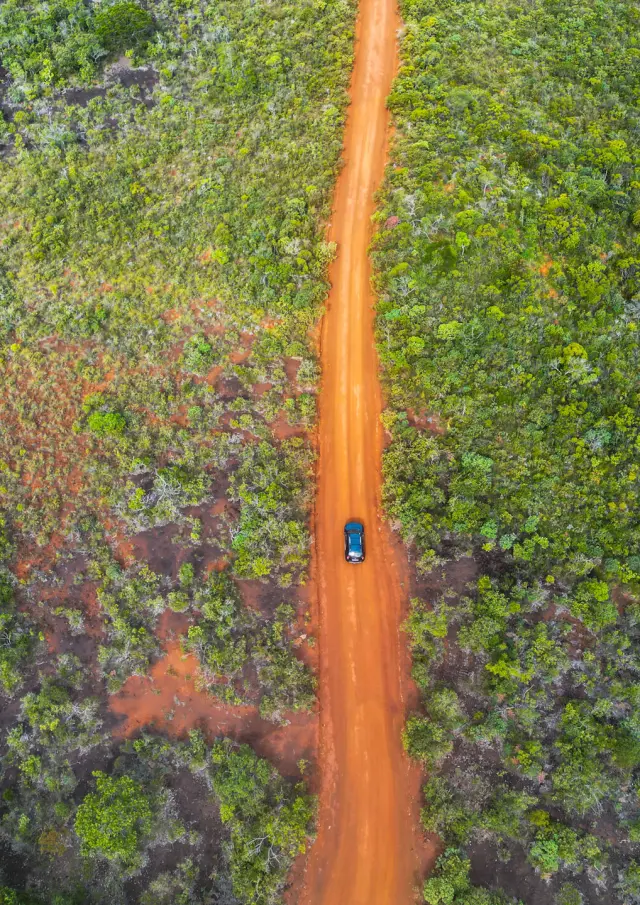 Vue aérienne d’une voiture sur une piste de terre rouge traversant la végétation du Grand Sud de la Nouvelle-Calédonie.