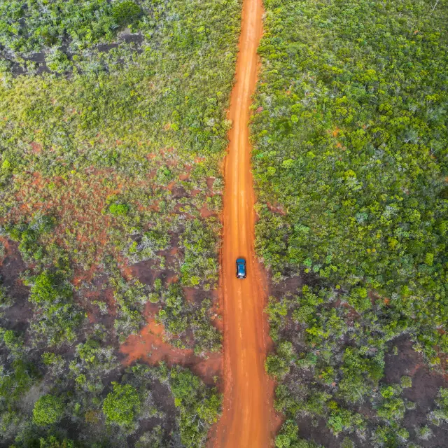 Aerial view of a car driving along a red dirt road through the vegetation of New Caledonia’s Great South.