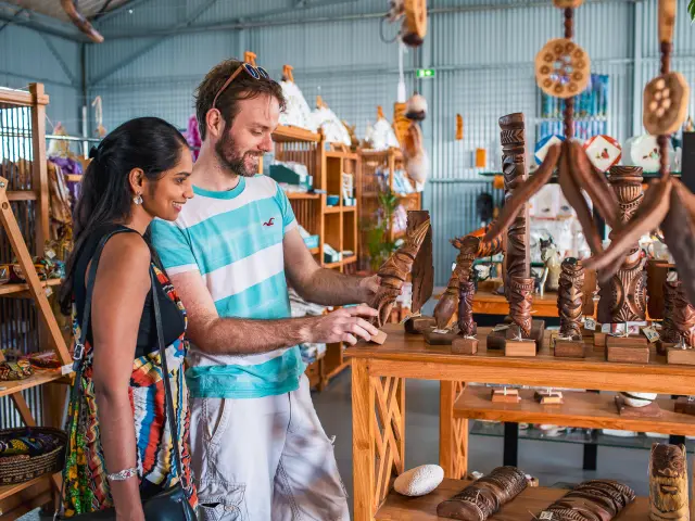 Deux visiteurs découvrent des sculptures en bois et des créations artisanales locales dans une boutique à Nouméa.