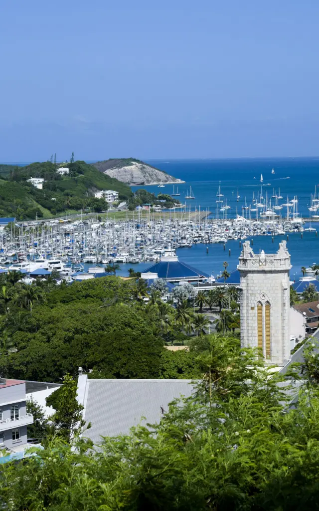 Vue panoramique sur la marina de Port Moselle à Nouméa, avec de nombreux voiliers, la cathédrale et le lagon en arrière-plan.