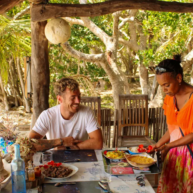Traveller seated at Gîte Kejaon in Poum while a local meal is served in a shaded natural setting.