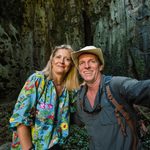 Un couple australien pose dans une grotte de Lifou, entouré de hautes parois rocheuses et d’une végétation humide.