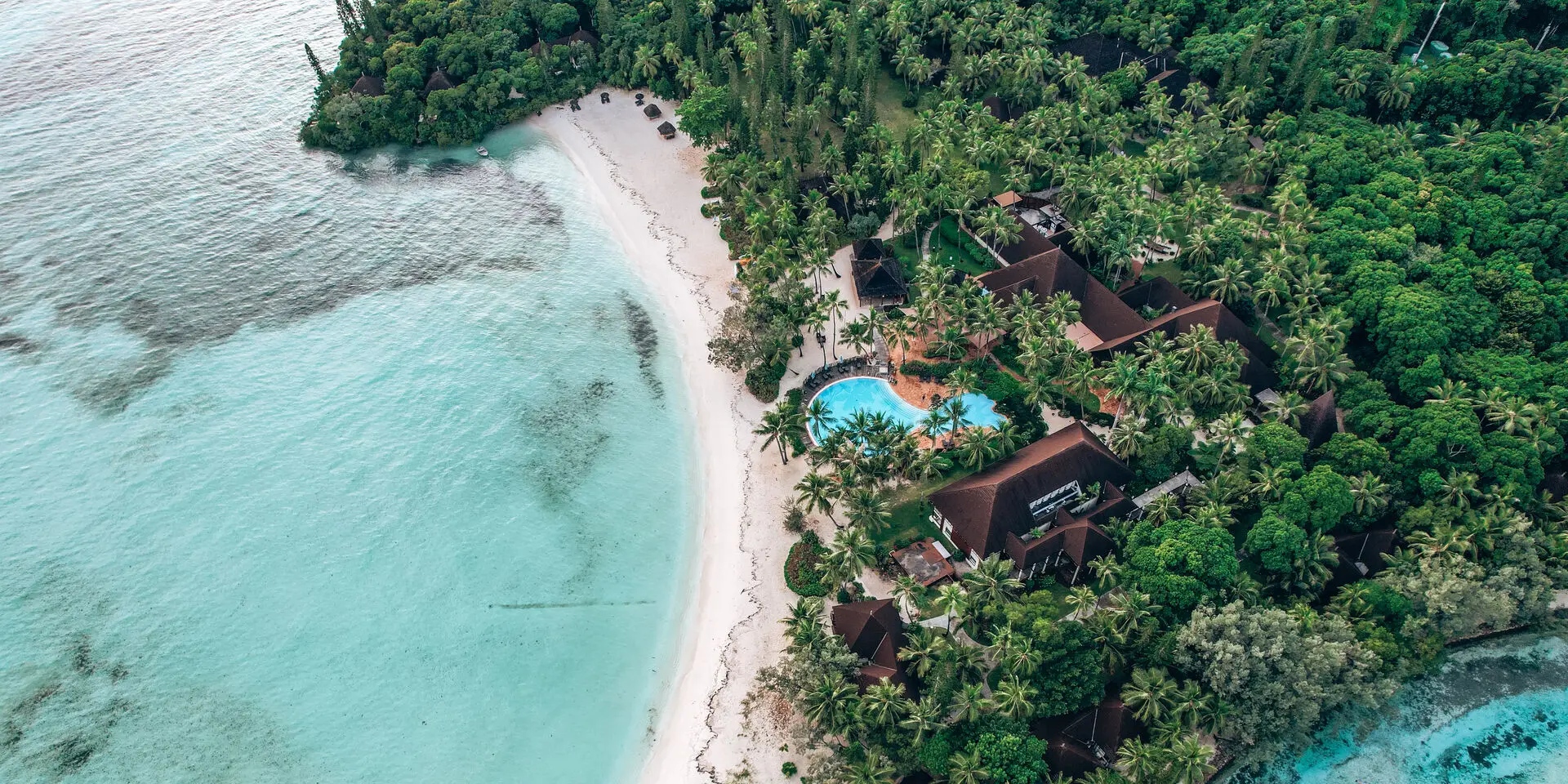 Vue aérienne sur Le Domaine Oro, Series by Marriott à l’Île des Pins, bordé par une plage de sable blanc, un lagon turquoise et une végétation tropicale.