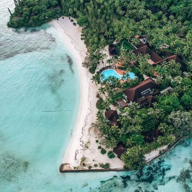 Aerial view of Domaine Oro, Series by Marriott on the Isle of Pines, bordered by a white-sand beach, turquoise lagoon and tropical vegetation.