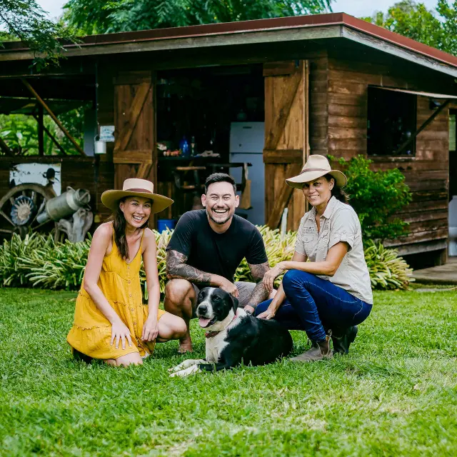 Des touristes singapouriens posent avec une hôte locale et un chien devant une maison en bois, lors d’une immersion en Brousse.