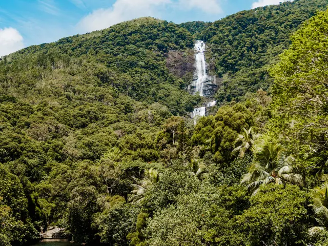 Vue de la cascade de Tao dévalant la montagne au-dessus d’une forêt tropicale, avec une rivière au premier plan à Hienghène.