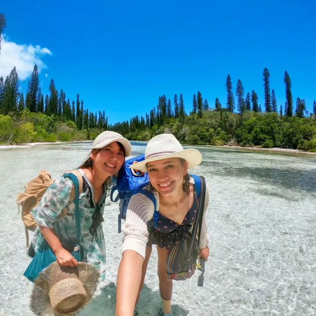Deux touristes japonaises sourient dans les eaux cristallines de la piscine naturelle d’Oro, à l’Île des Pins, entourées de pins colonnaires.
