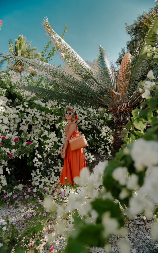 Une femme en robe orange pose au milieu de fleurs blanches et de feuillages tropicaux à Ouvéa, lors d’un shooting photo.