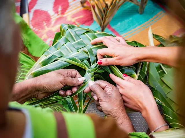 Des mains tressent des feuilles de pandanus pour réaliser un ouvrage artisanal, en Nouvelle-Calédonie.