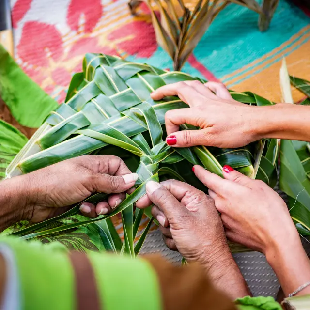 Des mains tressent des feuilles de pandanus pour réaliser un ouvrage artisanal, en Nouvelle-Calédonie.
