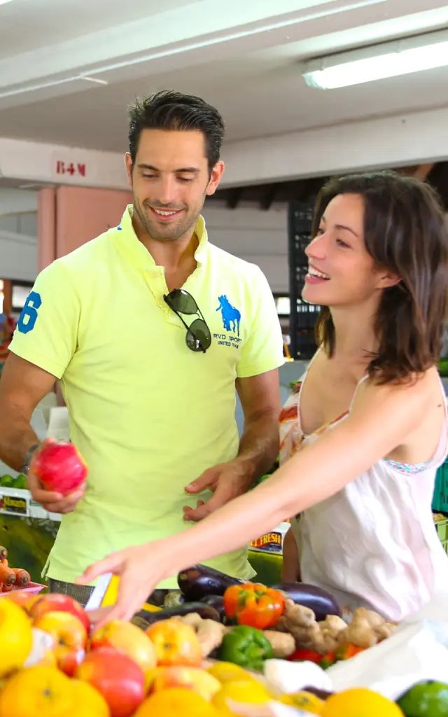 Un couple choisit des fruits et légumes sur un étal coloré au marché de Nouméa, en Nouvelle-Calédonie.