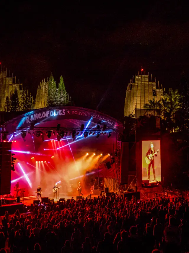 Nighttime Francofolies concert at the Tjibaou Cultural Centre in Noumea, with stage lights, large screens and a crowd in front of the stage.