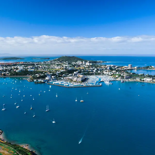 Vue aérienne de Nouméa : la ville, ses baies et de nombreux voiliers au mouillage dans un lagon bleu.