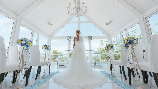 A bride in a white gown stands in a bright hotel chapel in Nouméa, decorated with white, blue and yellow flowers.