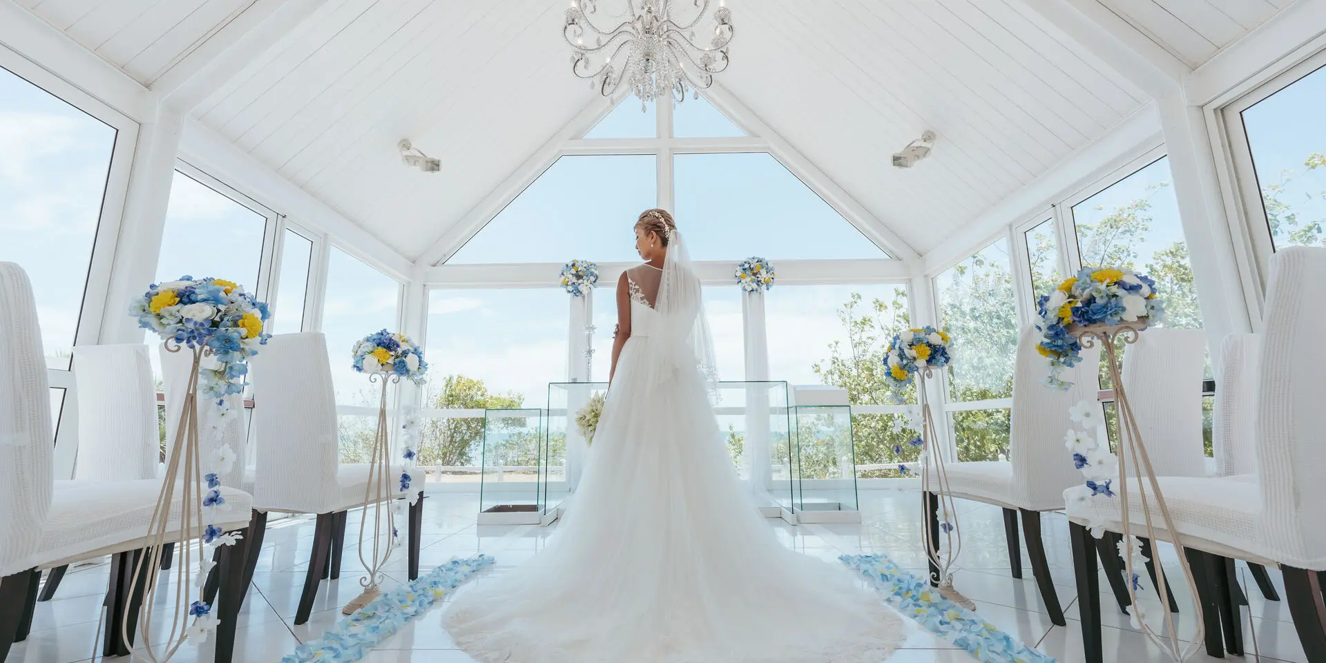 A bride in a white gown stands in a bright hotel chapel in Nouméa, decorated with white, blue and yellow flowers.