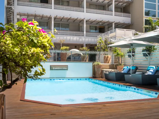 Swimming pool at Hôtel Le Lagon in Nouméa, surrounded by sun loungers, umbrellas and tropical greenery in an urban setting.