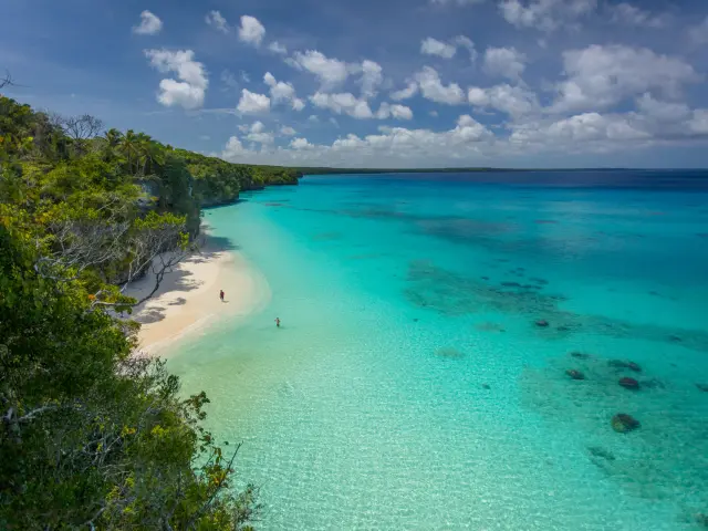 Vue sur la plage de Kiki à Lifou, avec son sable clair, son lagon turquoise et la végétation en bord de falaise.