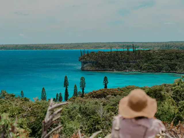 Vue sur la baie de Jinek à Lifou depuis la chapelle Notre-Dame de Lourdes, avec un lagon turquoise et une personne de dos au premier plan.