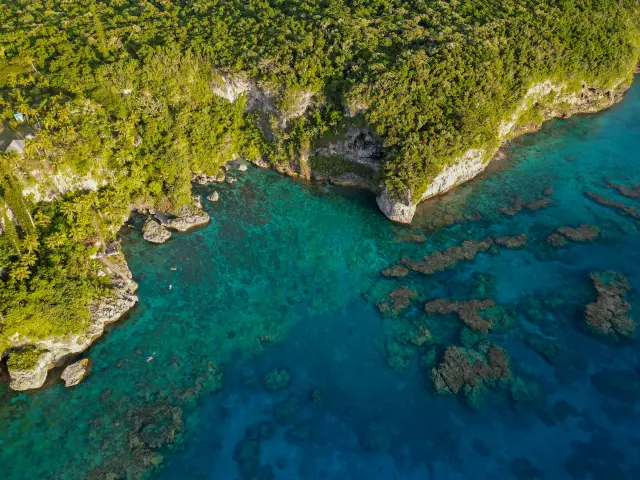 Vue aérienne des falaises de Jokin, entre végétation dense, falaises calcaires et eaux turquoise bordées de corail.