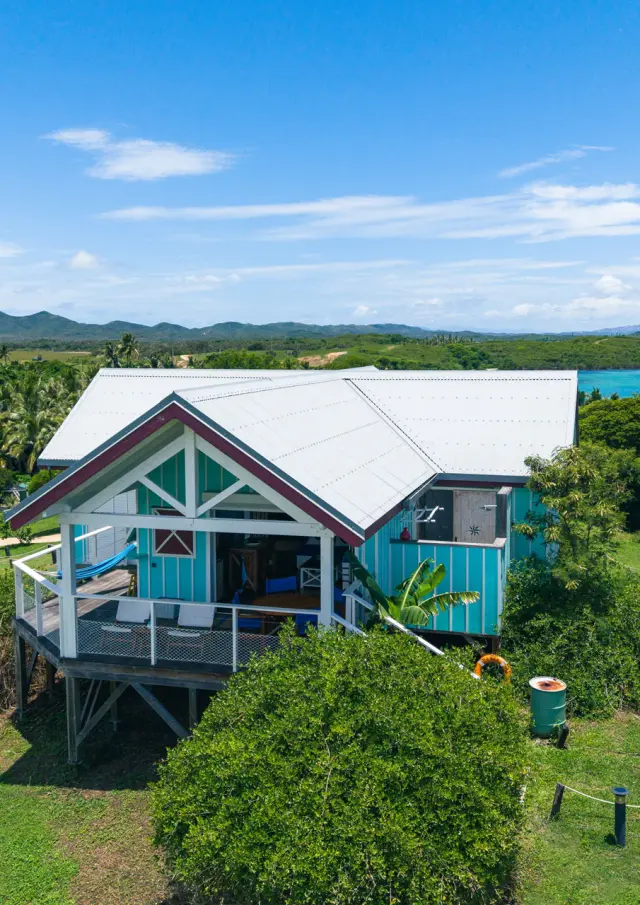 Vue d’une villa du Beach House Lodge à Poum, entourée de verdure avec le lagon en arrière-plan.