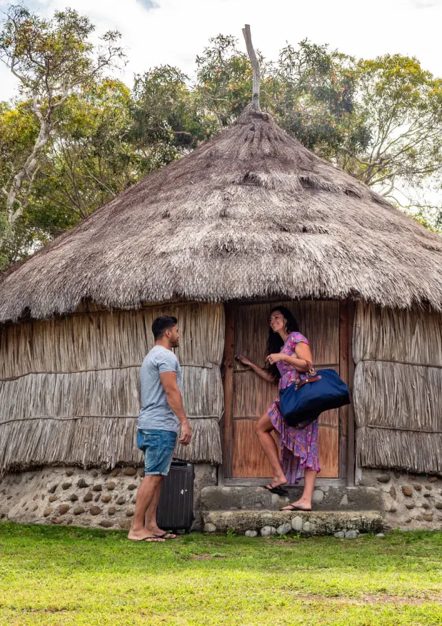 Couple arrivant avec des bagages devant La Case de Bouloup’ à Boulouparis, un hébergement inspiré de la case traditionnelle, entouré de nature.
