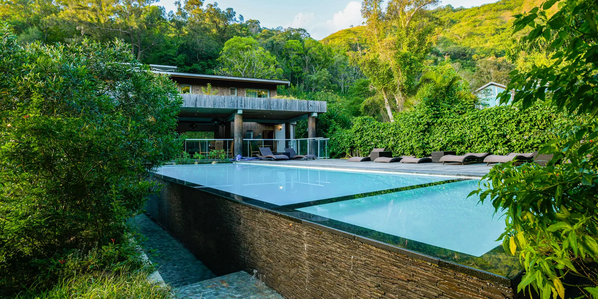 Piscine extérieure du Betikuré Parc Lodge à Bourail, entourée de transats, de végétation tropicale et de collines verdoyantes.