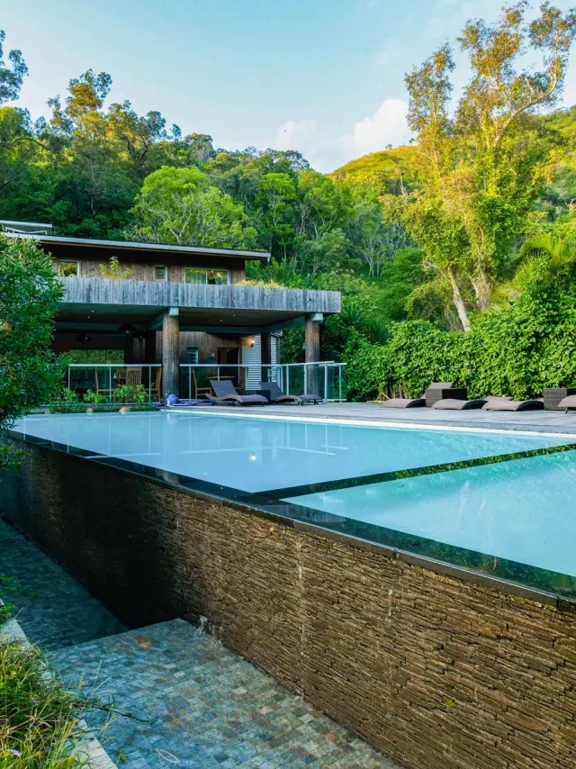 Piscine extérieure du Betikuré Parc Lodge à Bourail, entourée de transats, de végétation tropicale et de collines verdoyantes.