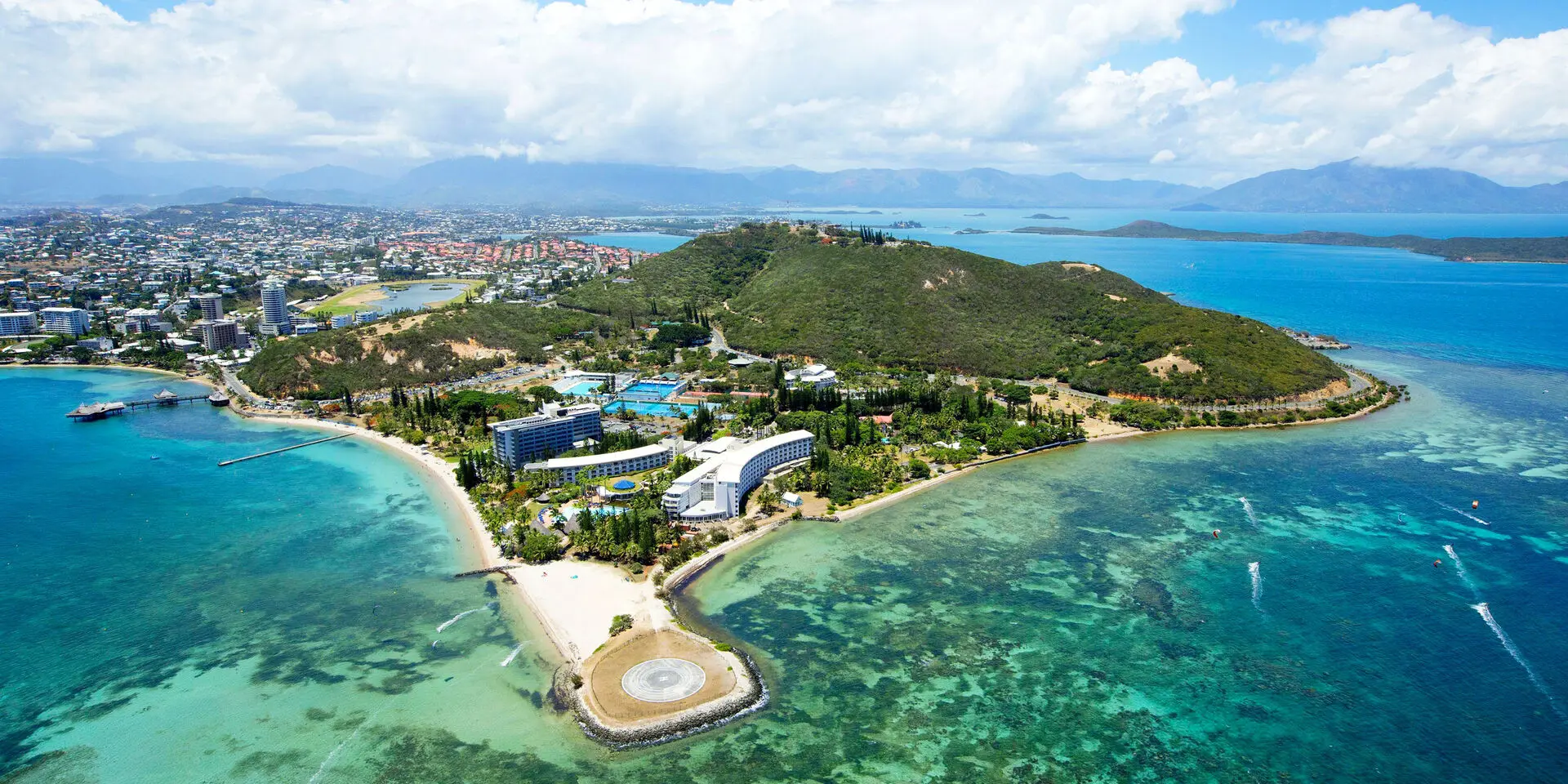 Aerial view of Nouméa Resort & Spa by the lagoon, with Anse Vata beaches, Nouméa peninsula and turquoise waters in the background.