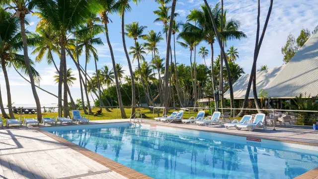 Piscine du Koulnoué Village à Hienghène, entourée de transats, de cocotiers et de bâtiments au style tropical en bord de mer.