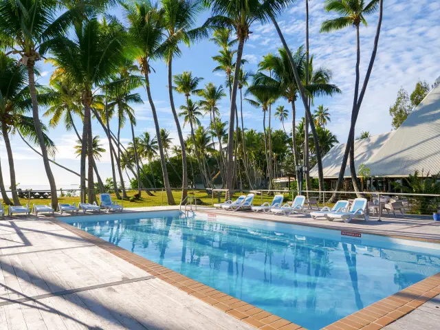 Swimming pool at Koulnoué Village in Hienghène, surrounded by sun loungers, coconut palms and tropical-style buildings by the sea.