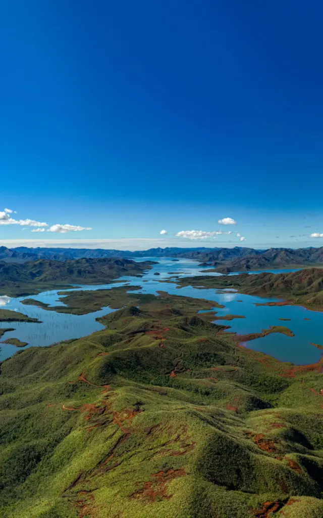 ブルーリバー州立公園のパノラマ。湖、緑の丘、グラン・スッドの赤土の風景、澄んだ青空が広がっている。