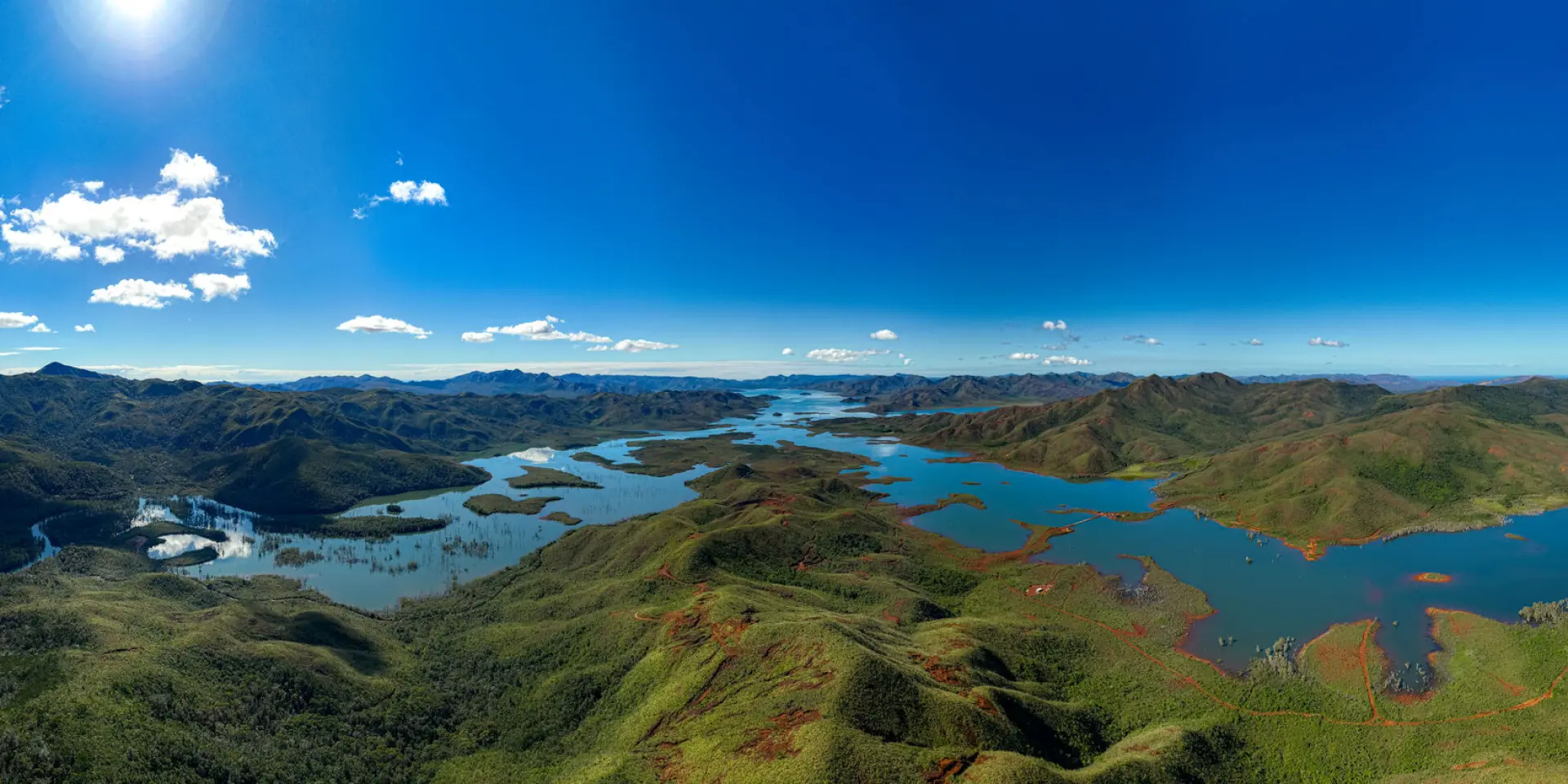 Vue panoramique du Parc provincial de la Rivière Bleue, avec lacs, collines verdoyantes, terres rouges du Grand Sud et ciel bleu dégagé.