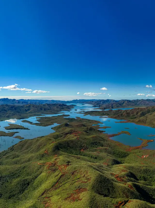 Vue panoramique du Parc provincial de la Rivière Bleue, avec lacs, collines verdoyantes, terres rouges du Grand Sud et ciel bleu dégagé.