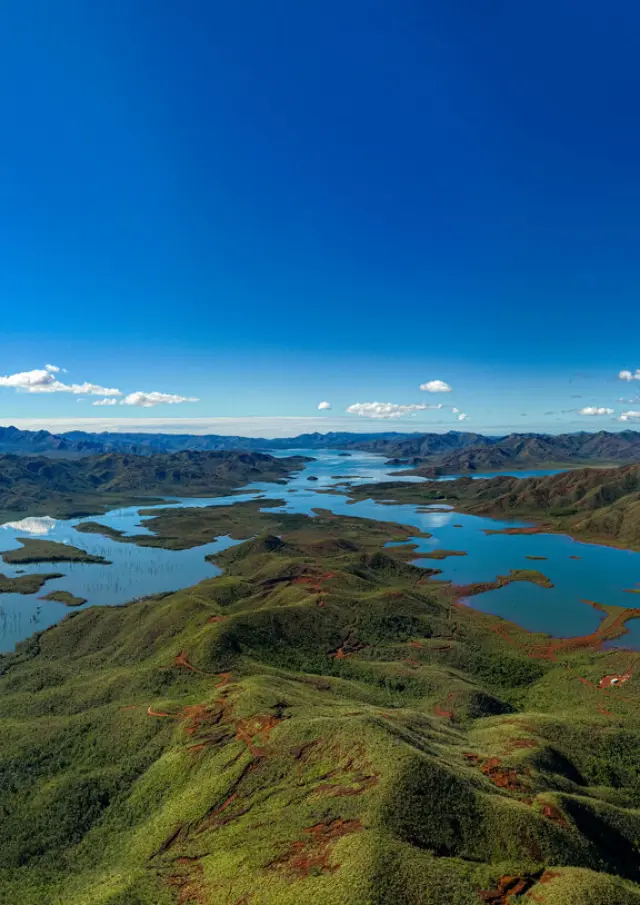 Vue panoramique du Parc provincial de la Rivière Bleue, avec lacs, collines verdoyantes, terres rouges du Grand Sud et ciel bleu dégagé.